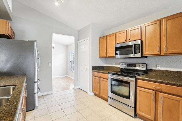 kitchen featuring light tile patterned flooring, dark stone countertops, lofted ceiling, and appliances with stainless steel finishes