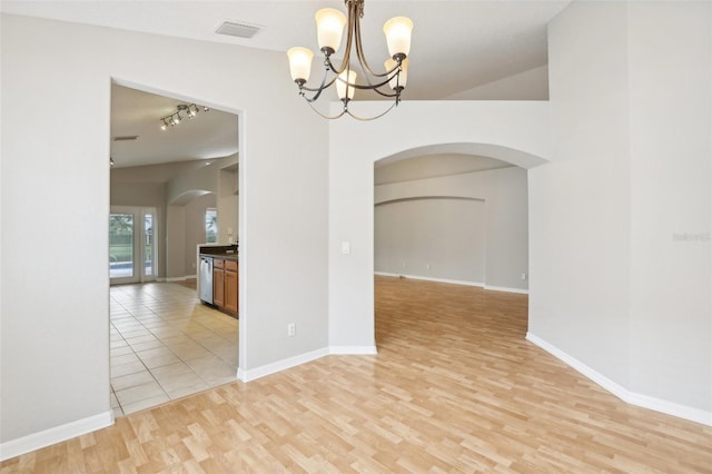 empty room featuring a chandelier, track lighting, light hardwood / wood-style floors, and vaulted ceiling