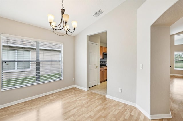 empty room with a chandelier, light hardwood / wood-style floors, and vaulted ceiling