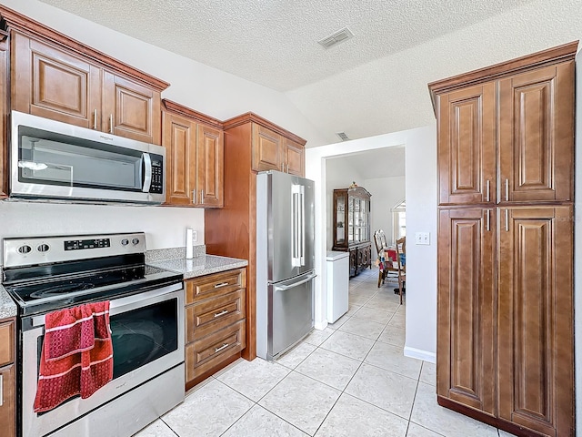 kitchen featuring light tile patterned floors, stainless steel appliances, a textured ceiling, and vaulted ceiling