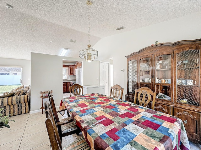 tiled dining space featuring a notable chandelier, a healthy amount of sunlight, a textured ceiling, and vaulted ceiling