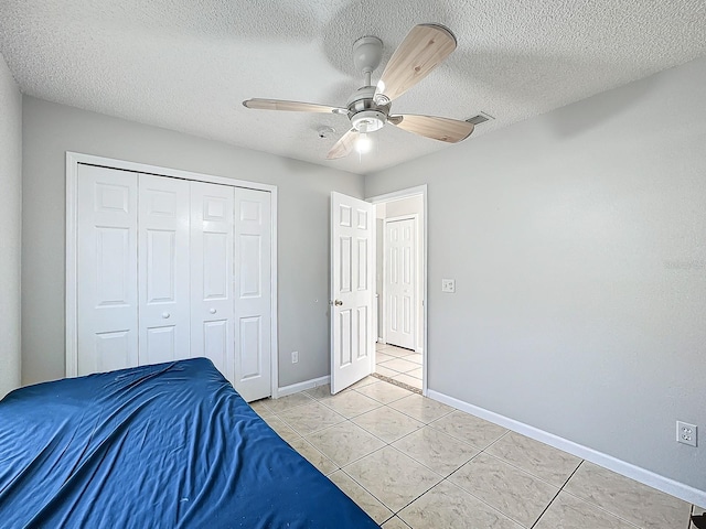 unfurnished bedroom with a closet, ceiling fan, a textured ceiling, and light tile patterned floors