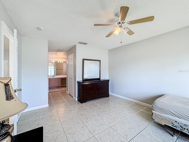 unfurnished bedroom featuring ceiling fan, a textured ceiling, light tile patterned floors, and ensuite bath