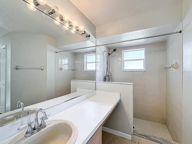 bathroom with a tile shower, tile patterned floors, a textured ceiling, and vanity