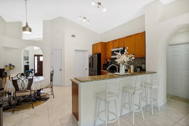 kitchen featuring kitchen peninsula, stainless steel appliances, decorative light fixtures, light tile patterned floors, and light stone counters