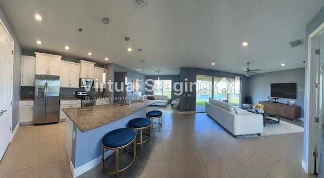 kitchen featuring stainless steel appliances, light tile patterned flooring, a kitchen bar, white cabinetry, and ceiling fan