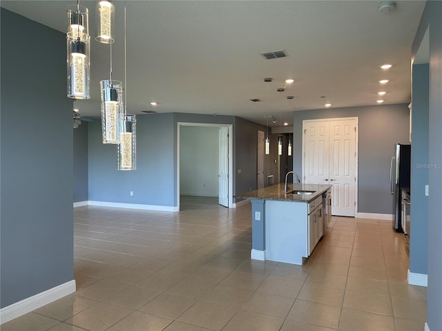 kitchen featuring a center island with sink, hanging light fixtures, dark stone counters, stainless steel refrigerator, and sink