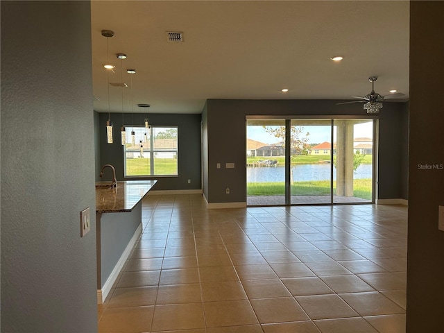 empty room featuring a water view, ceiling fan, light tile patterned floors, and plenty of natural light