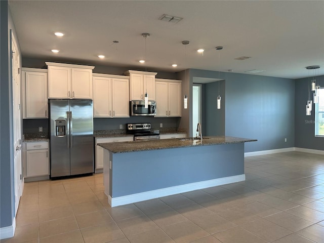 kitchen featuring stainless steel appliances, decorative light fixtures, a center island with sink, and white cabinets