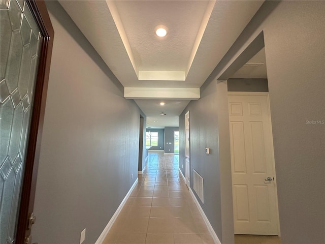 hallway featuring a tray ceiling, a textured ceiling, and light tile patterned floors