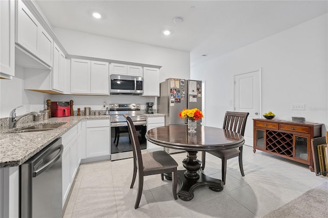 kitchen featuring appliances with stainless steel finishes, sink, white cabinetry, light stone counters, and light tile patterned floors