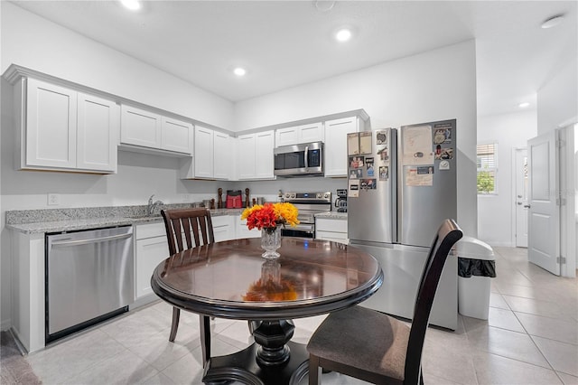 kitchen featuring appliances with stainless steel finishes, white cabinets, light stone countertops, and light tile patterned floors