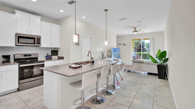 kitchen with appliances with stainless steel finishes, hanging light fixtures, ceiling fan, white cabinets, and a kitchen island with sink