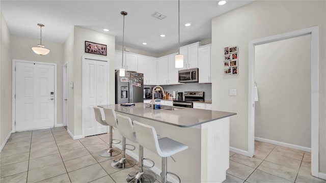 kitchen featuring appliances with stainless steel finishes, sink, white cabinetry, decorative light fixtures, and a kitchen island with sink