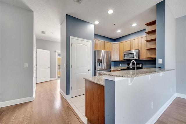 kitchen featuring kitchen peninsula, a kitchen bar, appliances with stainless steel finishes, light stone counters, and light hardwood / wood-style floors