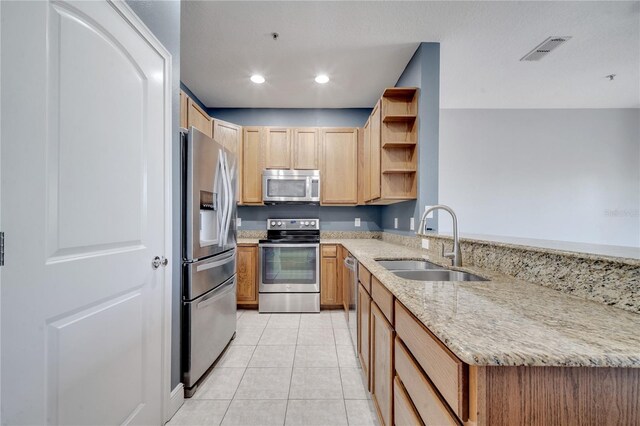 kitchen featuring kitchen peninsula, sink, light tile patterned floors, appliances with stainless steel finishes, and light stone counters