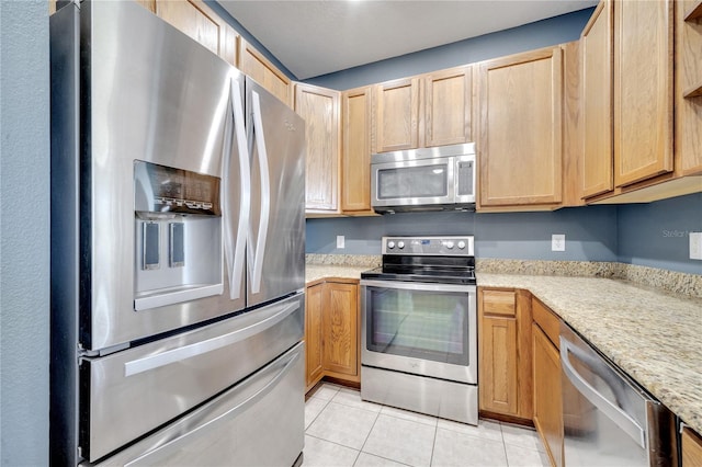 kitchen featuring light brown cabinetry, light tile patterned flooring, stainless steel appliances, and light stone countertops