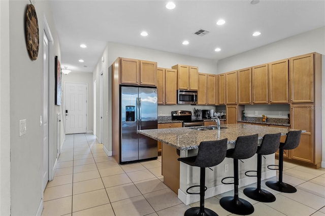 kitchen with visible vents, dark stone counters, a sink, stainless steel appliances, and a kitchen breakfast bar