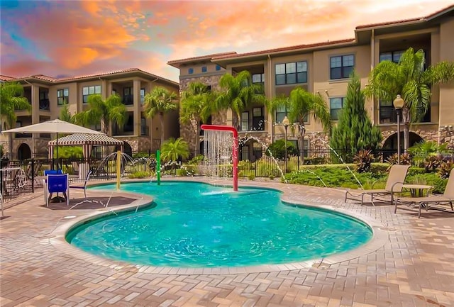 pool at dusk featuring a gazebo, pool water feature, and a patio area