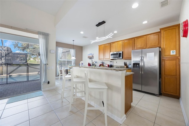 kitchen with stainless steel appliances, a center island, a kitchen bar, pendant lighting, and light tile patterned floors