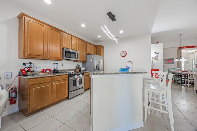 kitchen featuring appliances with stainless steel finishes, decorative light fixtures, a center island with sink, and light tile patterned floors