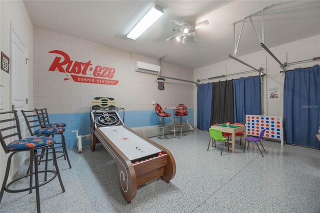 game room with ceiling fan, an AC wall unit, and a textured ceiling