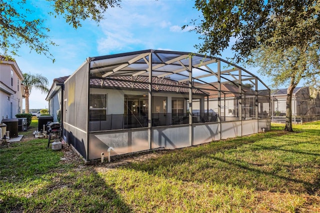 rear view of property featuring glass enclosure and a lawn