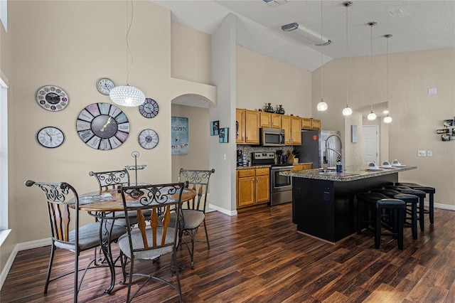 kitchen featuring stainless steel appliances, a breakfast bar area, a center island with sink, and hanging light fixtures