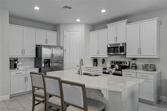 kitchen with sink, backsplash, white cabinetry, stainless steel appliances, and a center island with sink