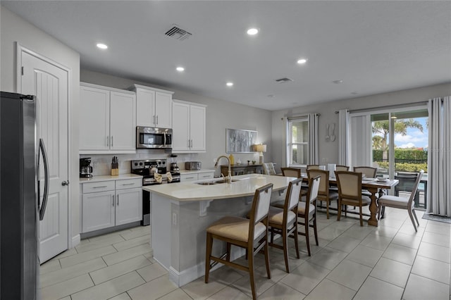 kitchen featuring appliances with stainless steel finishes, sink, a kitchen bar, white cabinets, and a center island with sink