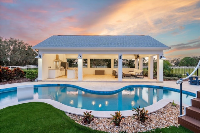 pool at dusk featuring a patio area, an outdoor kitchen, and a gazebo