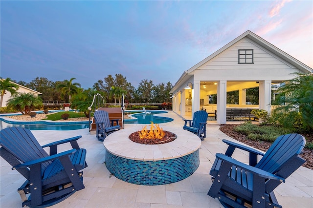 pool at dusk with an outdoor fire pit and a patio area