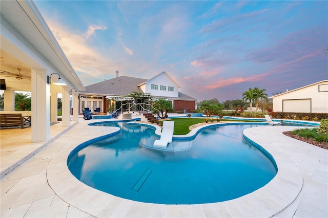 pool at dusk featuring ceiling fan and a patio area