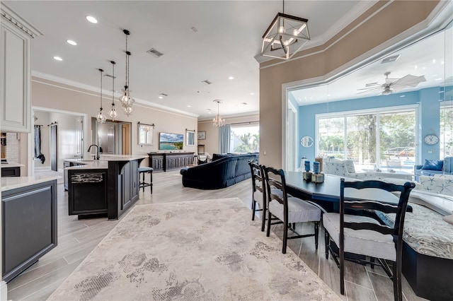 dining room featuring light hardwood / wood-style floors, sink, ornamental molding, and ceiling fan with notable chandelier