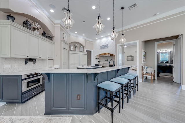 kitchen featuring a spacious island, hanging light fixtures, a breakfast bar, white cabinetry, and stainless steel oven