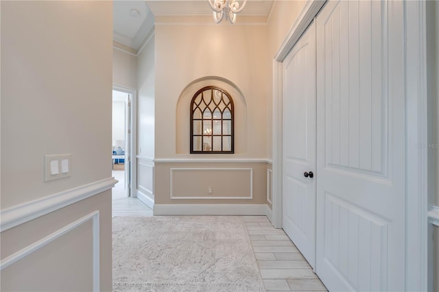 hallway with light hardwood / wood-style floors, an inviting chandelier, and crown molding