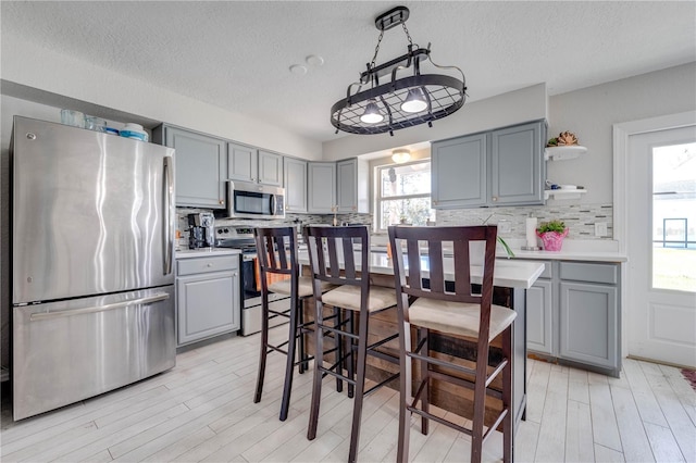 kitchen with stainless steel appliances, light hardwood / wood-style floors, backsplash, decorative light fixtures, and gray cabinets