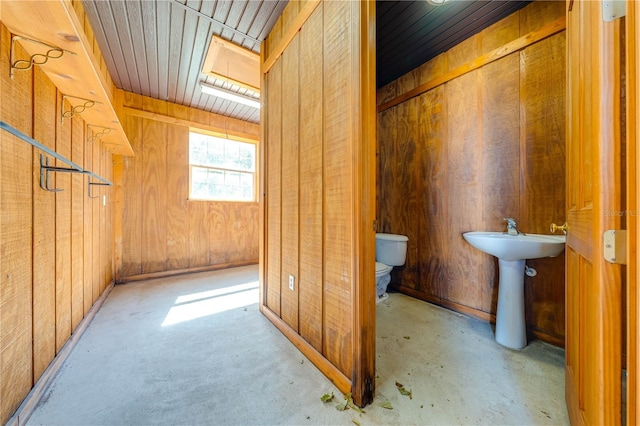 interior space with wooden walls, toilet, a skylight, and concrete floors