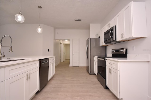 kitchen with appliances with stainless steel finishes, white cabinets, decorative light fixtures, and light hardwood / wood-style floors