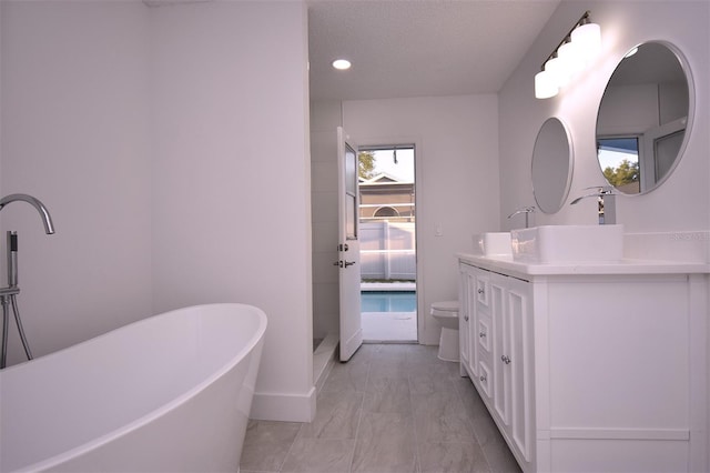 bathroom featuring toilet, a textured ceiling, vanity, and a tub to relax in