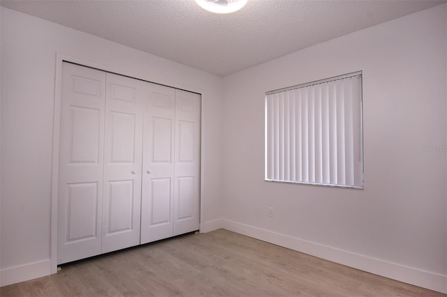 unfurnished bedroom featuring light hardwood / wood-style flooring, a textured ceiling, and a closet