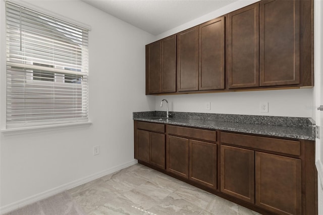 kitchen featuring dark brown cabinetry, dark stone counters, and sink