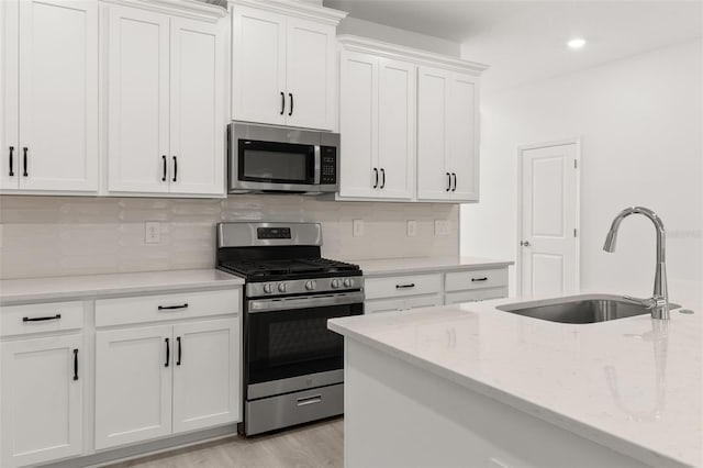 kitchen with white cabinetry, tasteful backsplash, light stone counters, light hardwood / wood-style flooring, and appliances with stainless steel finishes