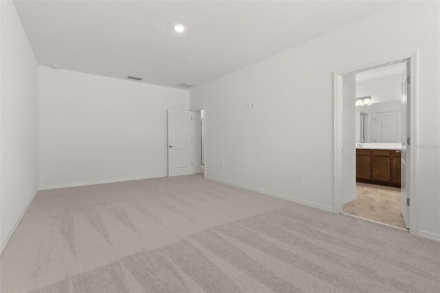 unfurnished bedroom featuring connected bathroom and light colored carpet