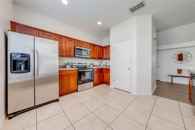kitchen with brown cabinets, light tile patterned flooring, appliances with stainless steel finishes, light countertops, and visible vents
