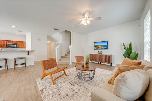 living room featuring stairway, light wood-style flooring, baseboards, and ceiling fan