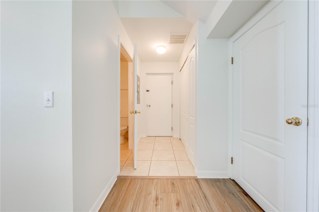 hallway featuring baseboards, light wood finished floors, and visible vents
