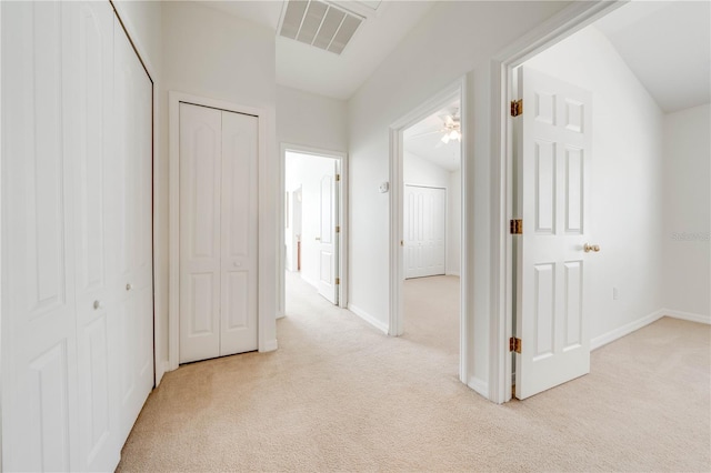 hallway featuring lofted ceiling, baseboards, visible vents, and light carpet