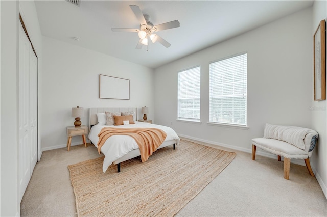 bedroom with baseboards, ceiling fan, a closet, and light colored carpet