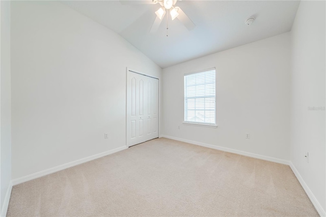 empty room with baseboards, a ceiling fan, vaulted ceiling, and light carpet